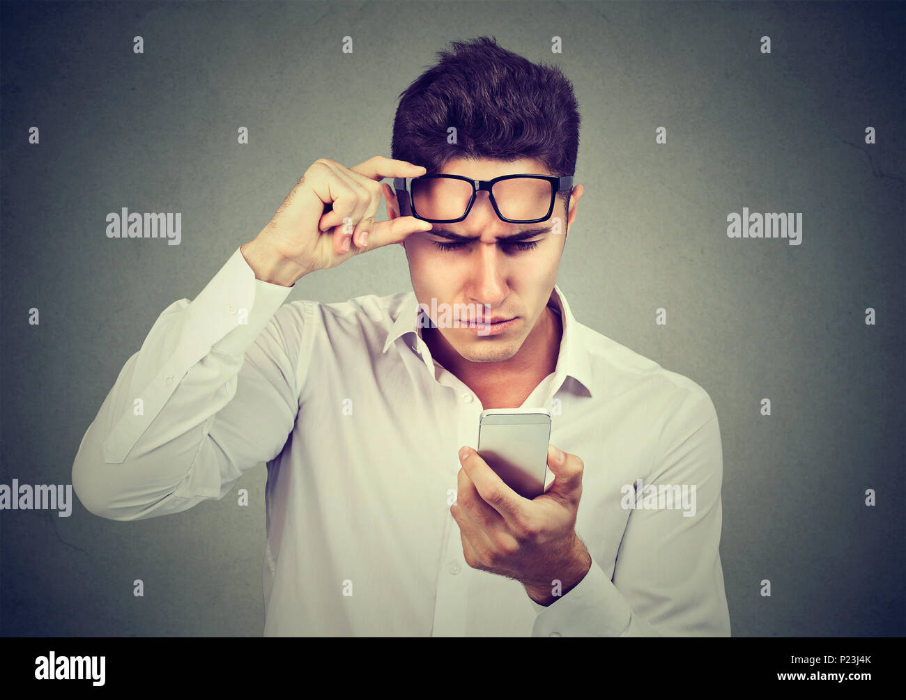 Giovane Uomo con occhiali aventi problemi a visualizzare cellulare ha problemi di visione. Bad messaggio di testo. Human percezione dell emozione Foto Stock