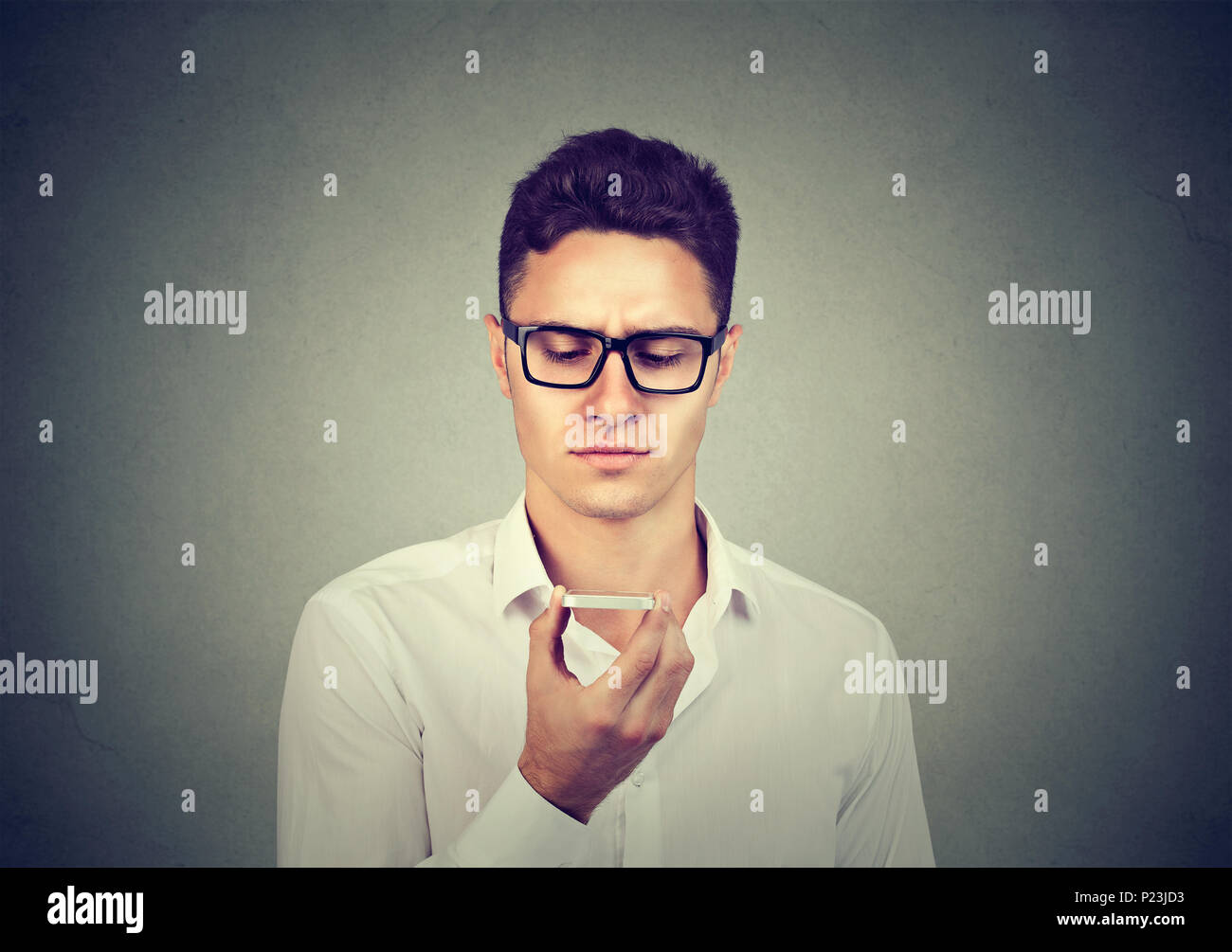 Uomo che utilizza un telefono intelligente funzione riconoscimento vocale sulla linea l'ascolto ai risultati della ricerca isolato sul muro grigio sfondo Foto Stock