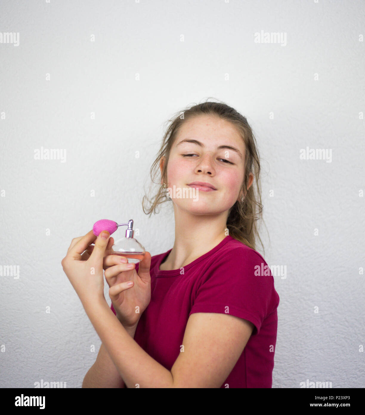 Bionda giovani adolescenti kid ragazza mettendo profumo sul suo lungo collo wxposed e a testa alta i capelli biondi e contenitore di rosa di buon profumo in studio. Foto Stock