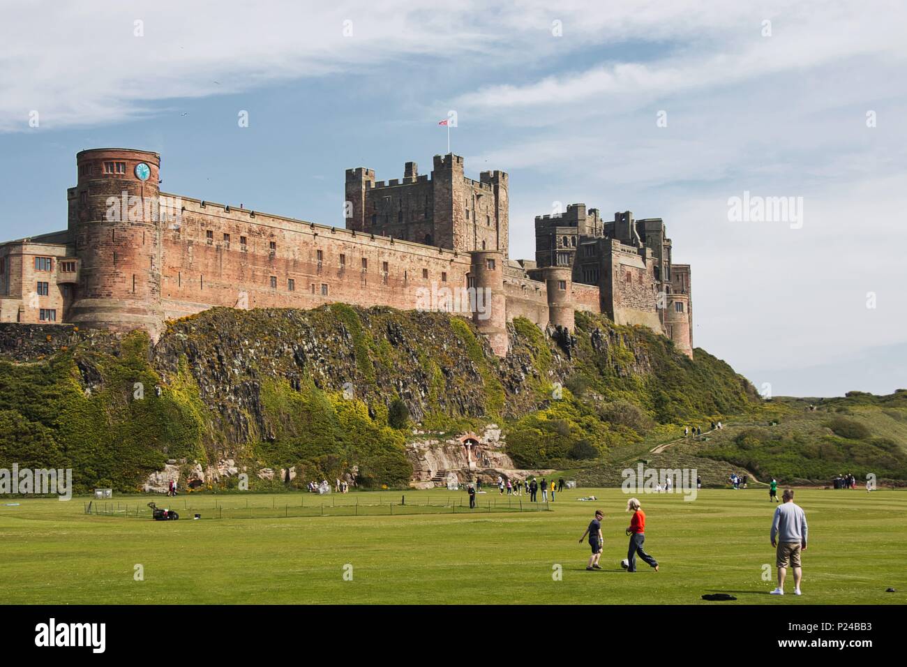Le famiglie a giocare sul campo sotto il castello di Bamburgh, Northumberland, Regno Unito Foto Stock