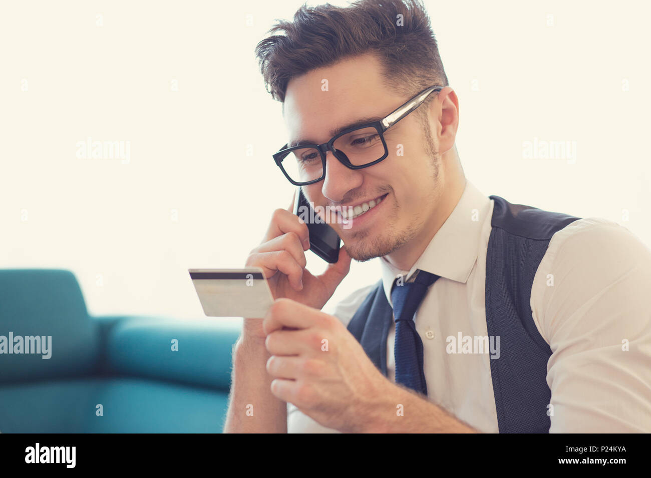 Giovane uomo bello in bicchieri di parlare al telefono e azienda carta di credito la prenotazione di un viaggio. Foto Stock