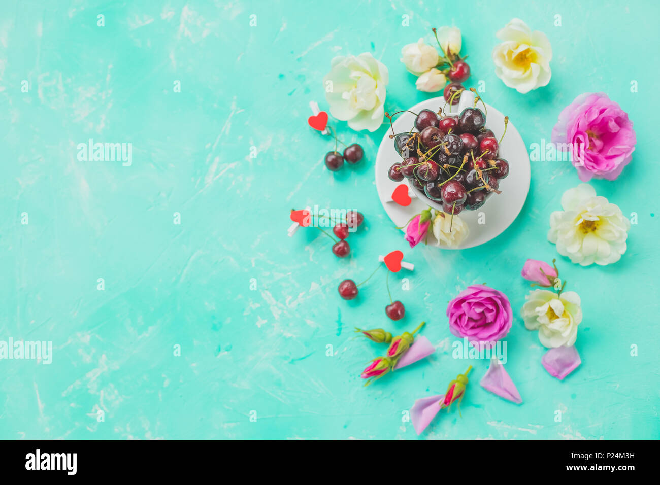 Tazza di erbe di bacche di ciliegio,rosa tea con mazzo di rose di diramazione ,olio essenziale. Le piante officinali e aromatiche composizione. Piano di composizione dei laici con deliziosi frutti di bosco. Spazio di copia Foto Stock