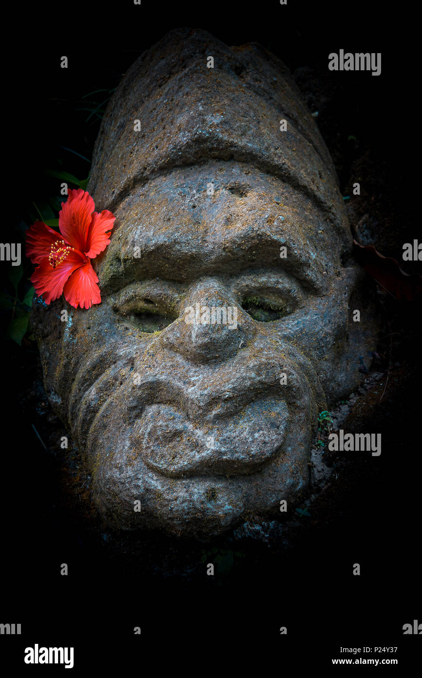 Antica pietra balinesian faccia con un rosso di fiori di ibisco dietro l'orecchio, Ubud, Bali, Aprile 14 2018 Foto Stock
