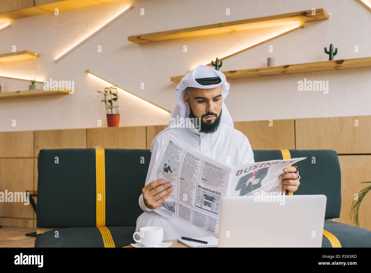 Giovane imprenditore musulmano leggendo il giornale in cafe Foto Stock