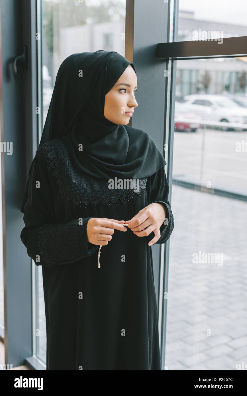Considerato giovane donna musulmana con grani di preghiera cercando in corrispondenza della finestra Foto Stock