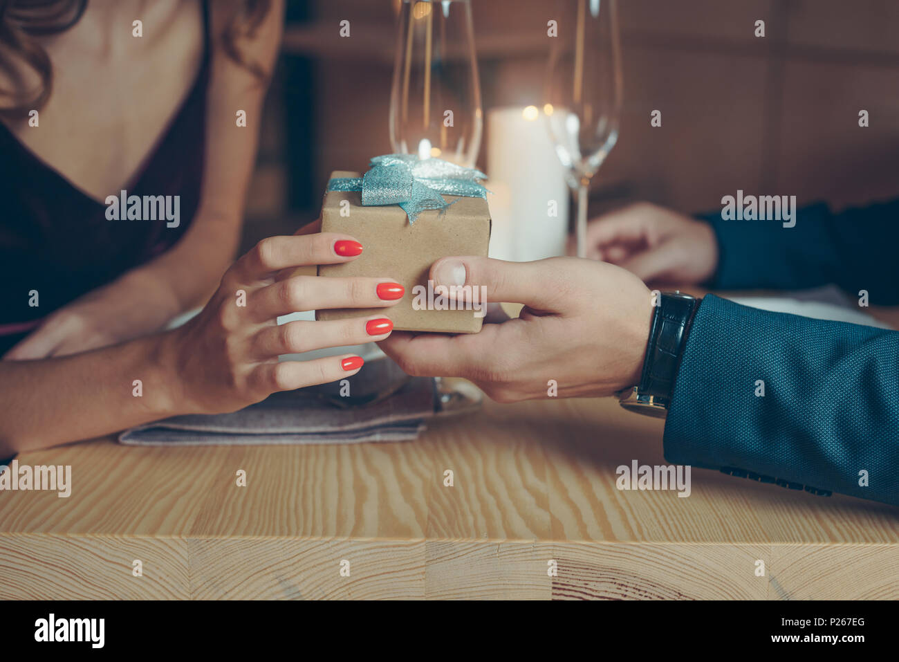 Ritagliato shot della giovane azienda avvolto confezione regalo durante una cena romantica nel ristorante Foto Stock