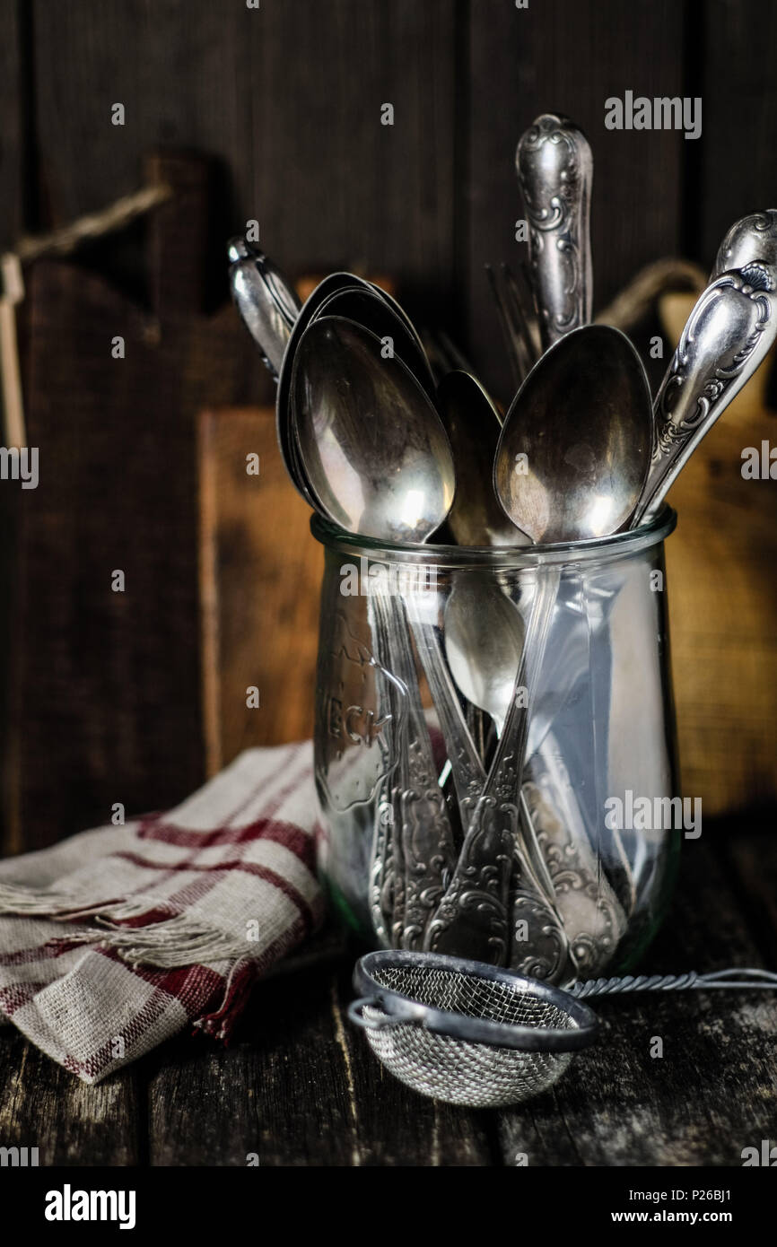 Vita Tranquilla con l'annata utensili di cucina: vecchie posate in argento in una wake-up, vetro vecchio crivello, biancheria e tavole di legno Foto Stock