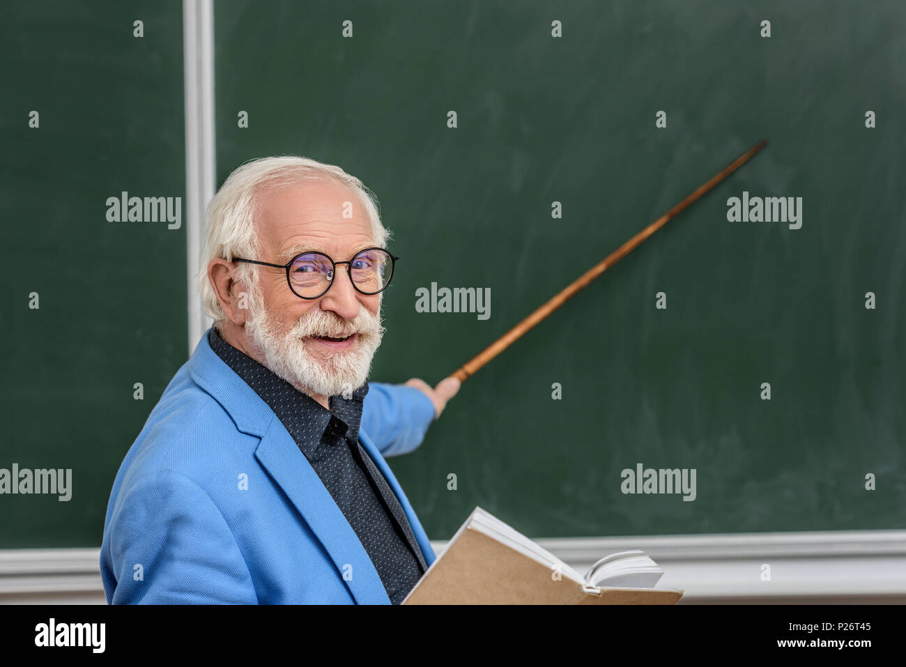 Capelli grigi professore azienda prenota e puntando su qualcosa di Blackboard Foto Stock