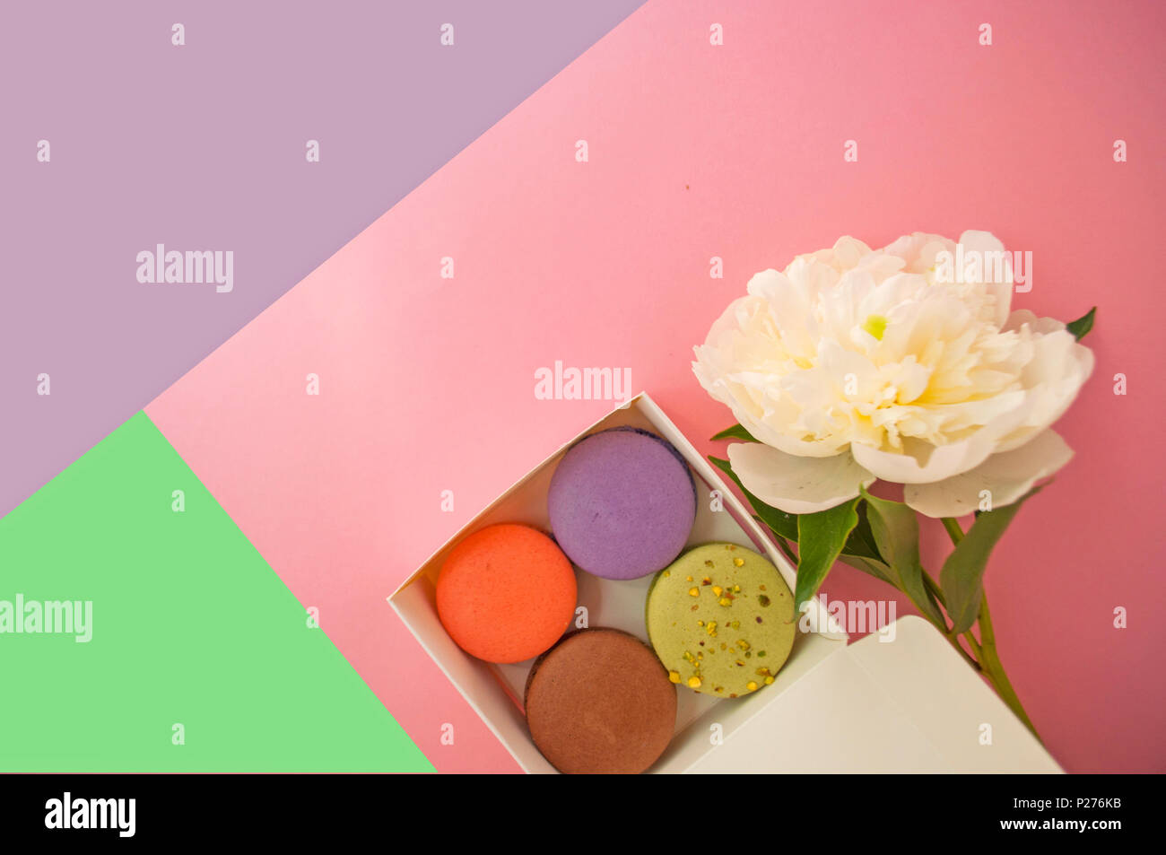 Colorato deliziosi dessert francesi macarons in una casella e un bel bianco peonia in rosa, viola e verde dello sfondo. Foto Stock