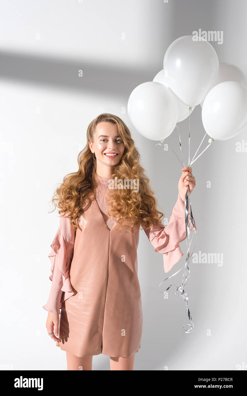 Felice ragazza in abito beige bundle di contenimento di palloncini con elio Foto Stock