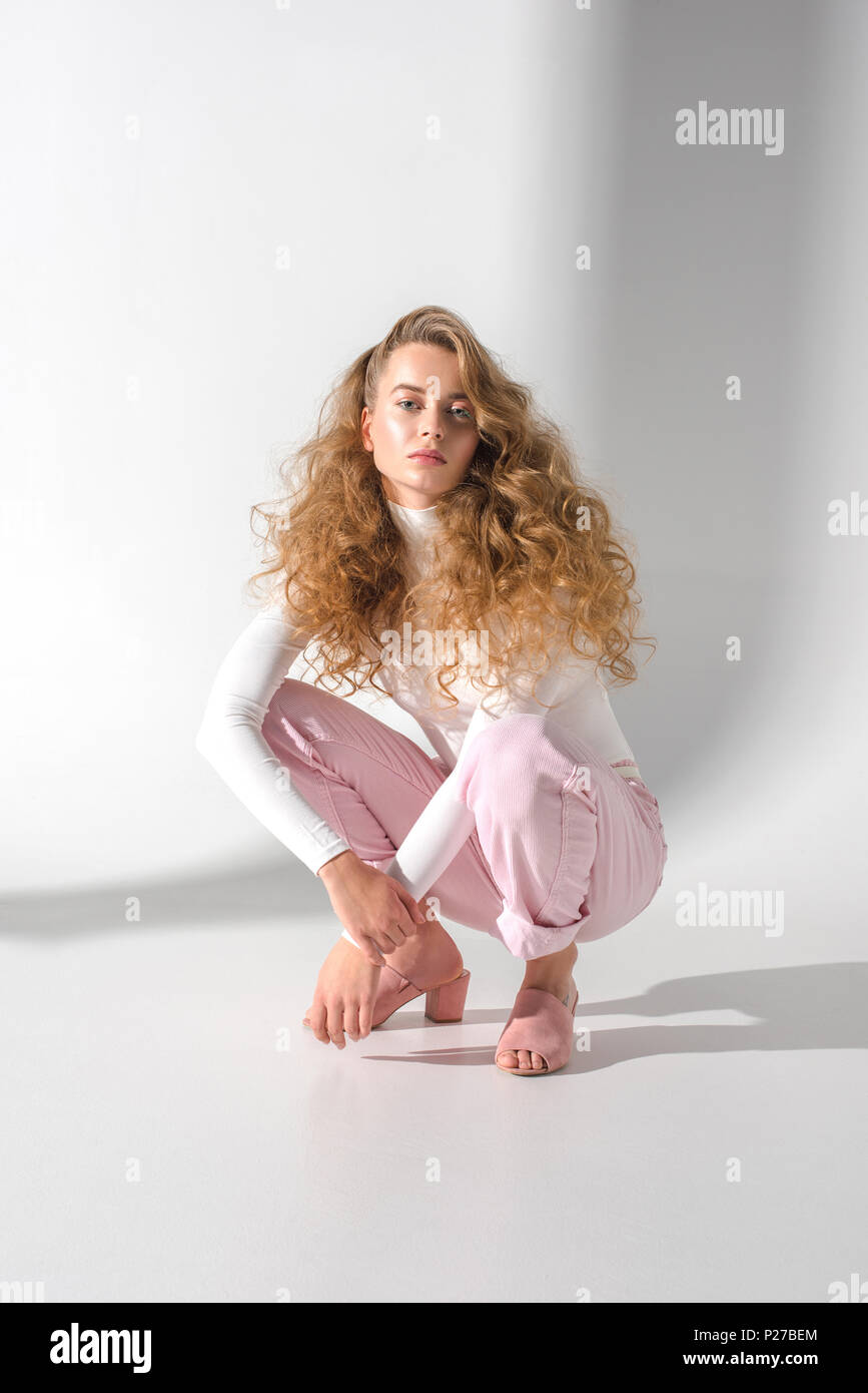 Bellissima ragazza con i capelli ricci accovacciata e guardando la  fotocamera Foto stock - Alamy