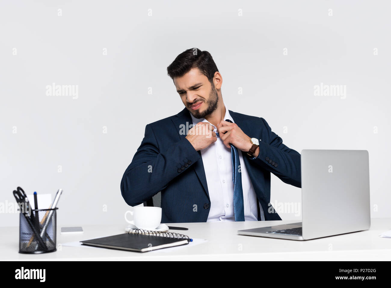 Giovane imprenditore oberato di lavoro regolazione della cravatta mentre è seduto al posto di lavoro Foto Stock