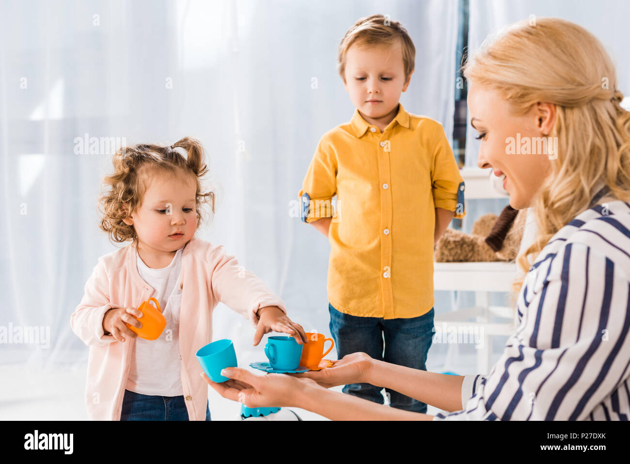 Figlio guardando come madre e sorella gioca con i bicchieri di plastica Foto Stock