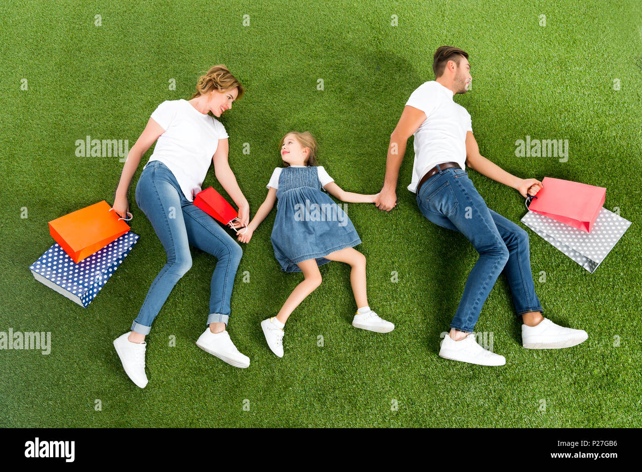 Vista aerea della famiglia sorridente con le borse della spesa tenendo le mani insieme su erba verde Foto Stock
