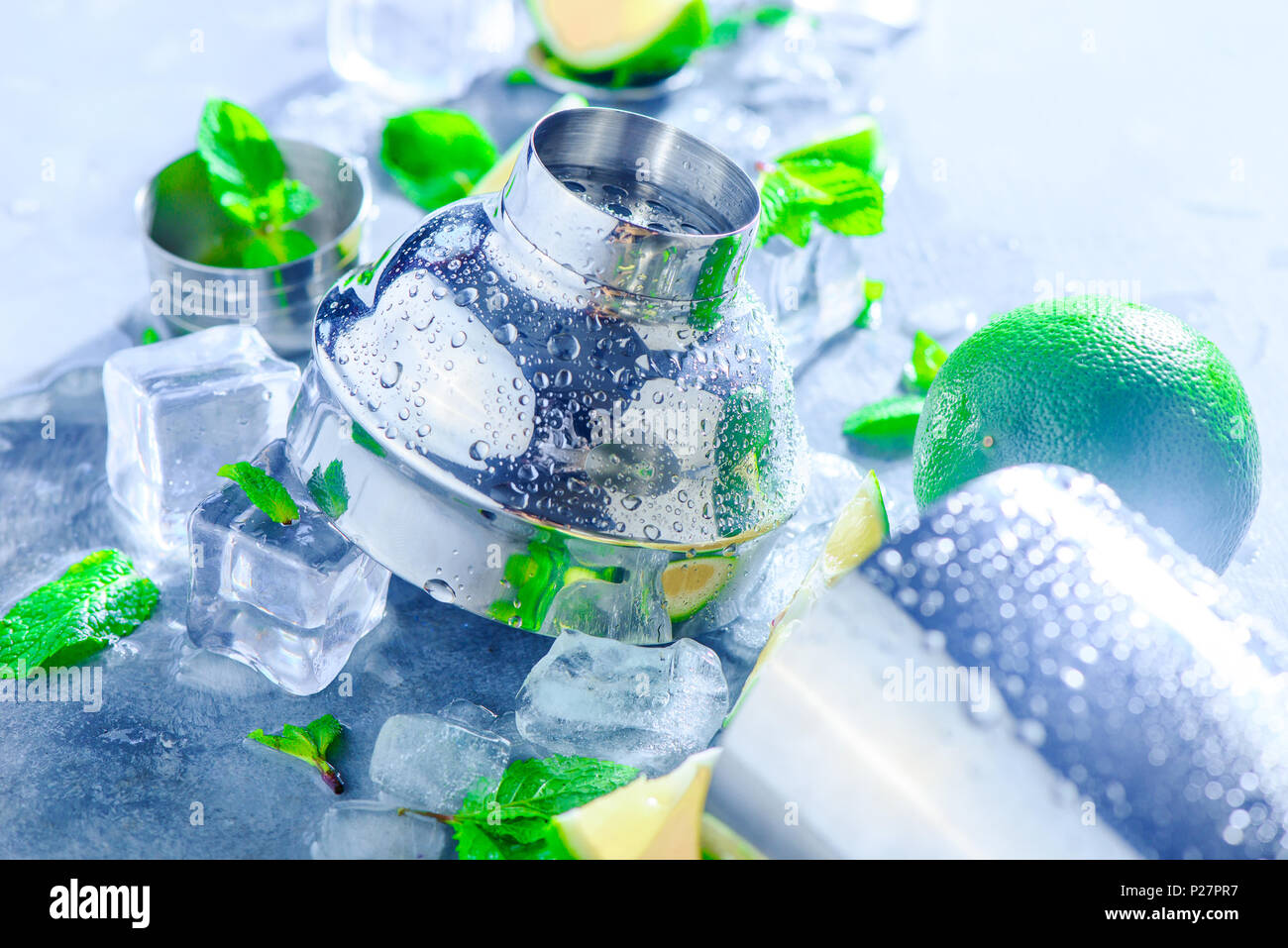 Shaker e accessori bar close-up. Cocktail Mojito ingredienti, menta, calce e cubetti di ghiaccio su una pietra grigia sullo sfondo. Bevanda estiva concetto con copia Foto Stock