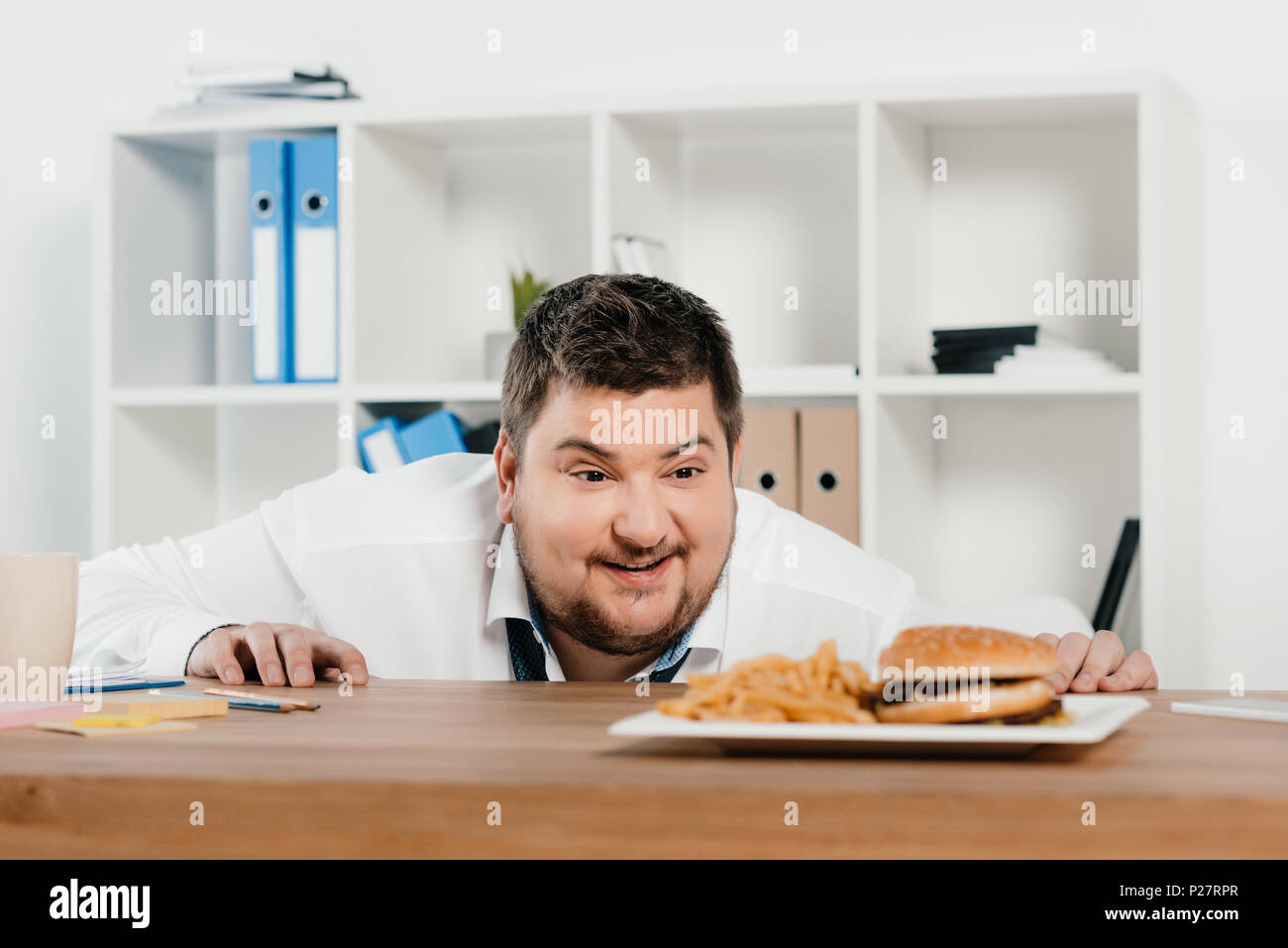 Il sovrappeso imprenditore guardando hamburger e patatine fritte in office Foto Stock