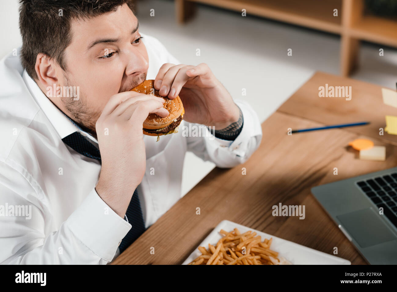 Imprenditore sovrappeso mangiare hamburger al lavoro Foto Stock