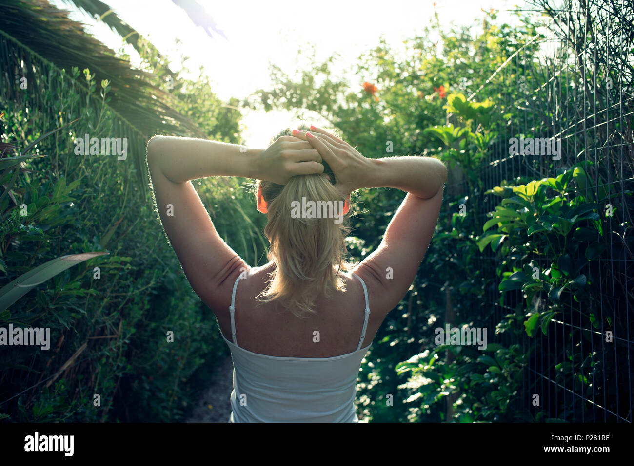 Vista posteriore della donna bionda che si immerse in qualche raggio per la vitamina D in un giardino sontuoso vicino a Punta del Este, Uruguay. Foto Stock