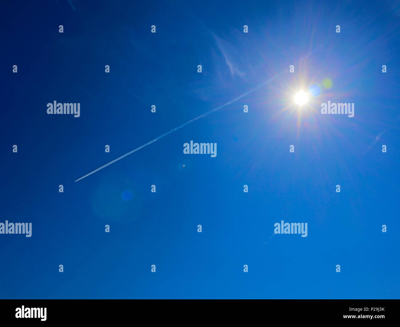 Sole brillante con razzi e spettrale aureola intorno contro il cielo blu bianco con tracce a getto Foto Stock