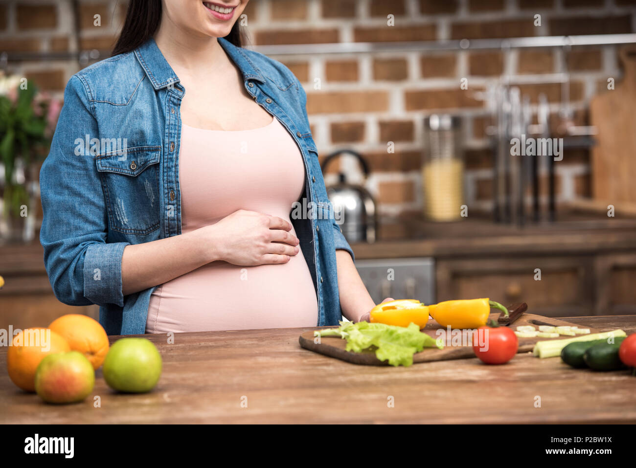 Ritagliato colpo di sorridente giovane donna incinta toccando ventre durante la cottura Foto Stock