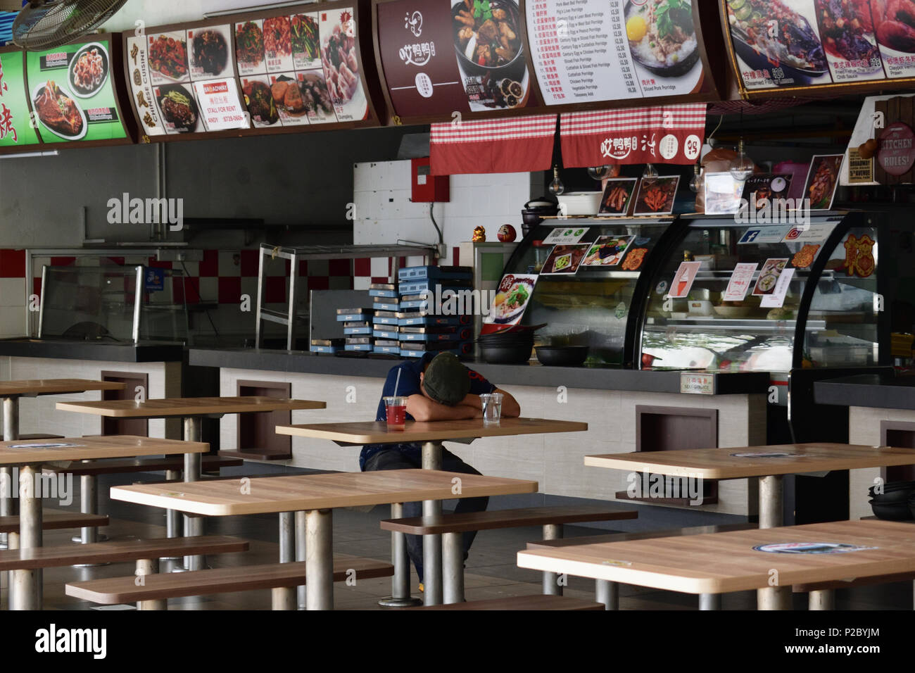 Singapore. Nelle prime ore del mattino, un lavoratore tiene un pisolino su una delle tabelle vuote in una ancora vuoto-coffee shop. Foto Stock