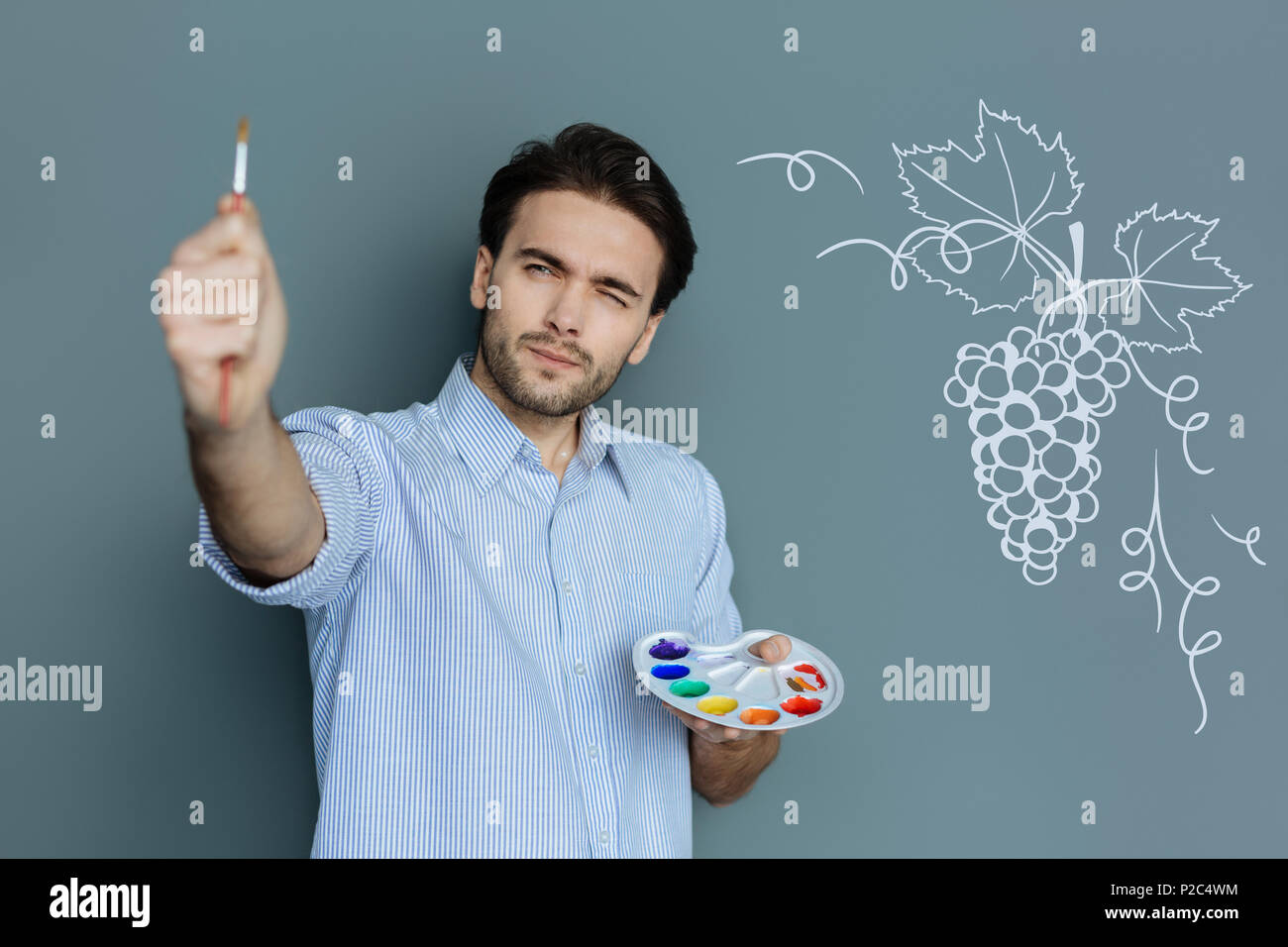 Pittore concentrato chiudendo un occhio osservando la spazzola Foto Stock