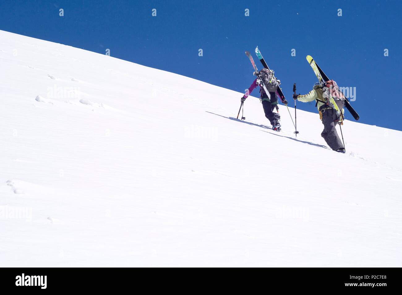 Una femmina e un maschio alpinista che trasportano i loro gli sci sulla loro zaini e salendo un ripido pendio di neve, vertice di Rocci Foto Stock
