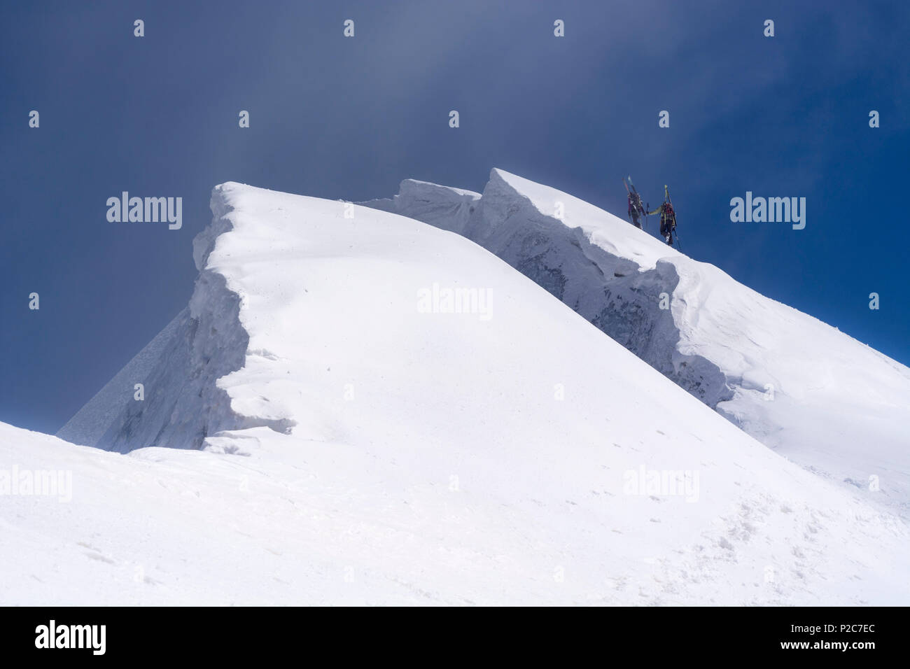 Una femmina e un maschio alpinista che trasportano i loro gli sci sulla loro zaini e salendo un ripido pendio di neve, accanto a loro bi Foto Stock