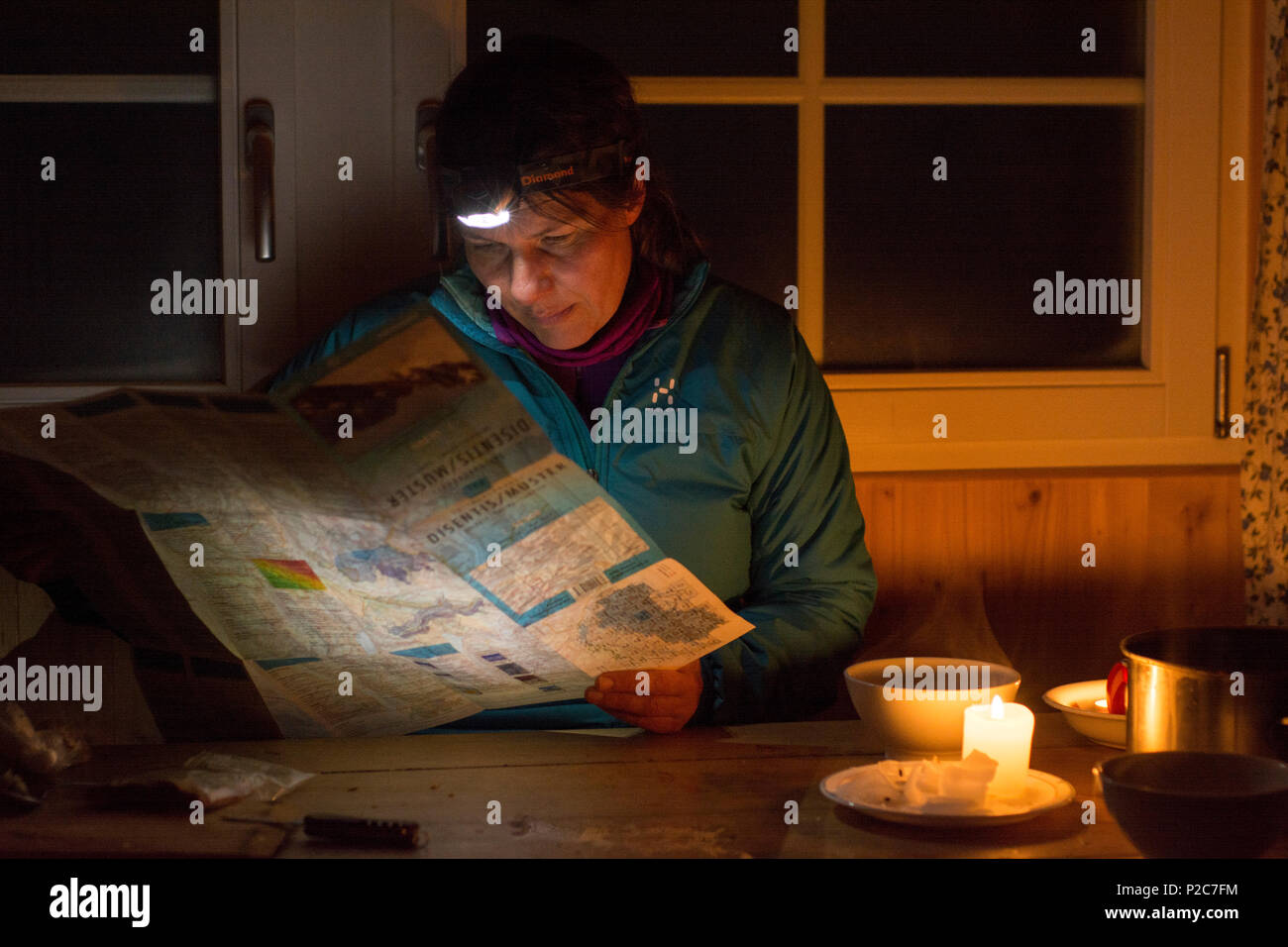 Una donna con un faro seduti ad un tavolo e guardando la mappa di scialpinismo nel lume di candela, Cadlimo capanna, valle denominato Val Cam Foto Stock