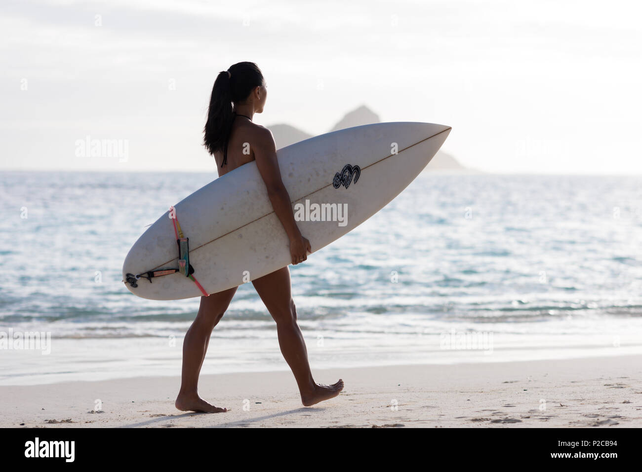 Donna che cammina con la tavola da surf in spiaggia Foto Stock