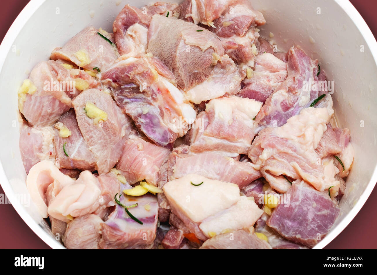 Raw Condite la carne di maiale in una ciotola. La carne di maiale condita con sale, aglio e rosmarino. La preparazione di pezzi di carne di maiale prima di friggere. Foto Stock