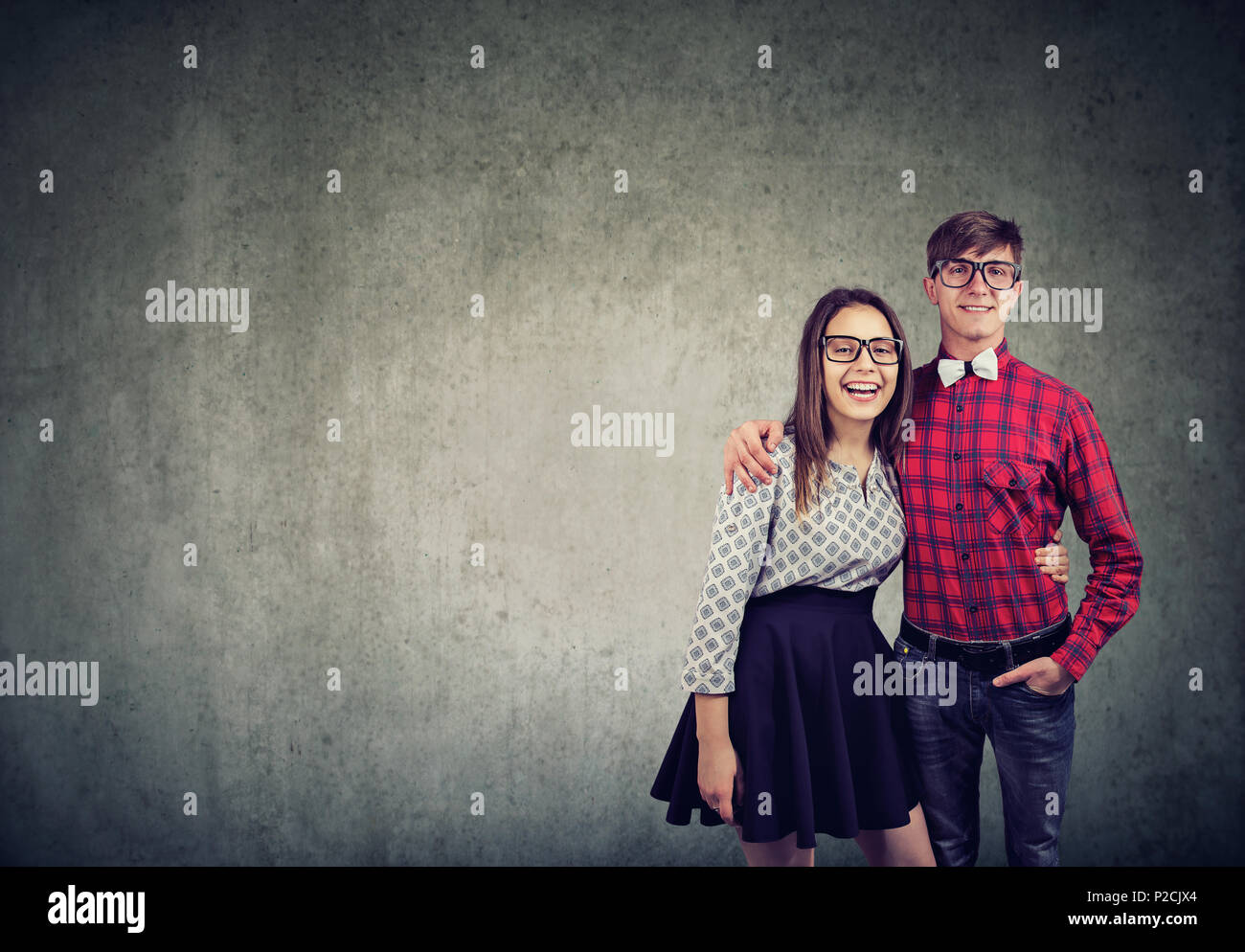 Ragazza casual e uomo in bicchieri abbracciando e ridere per fotocamera su sfondo grigio Foto Stock