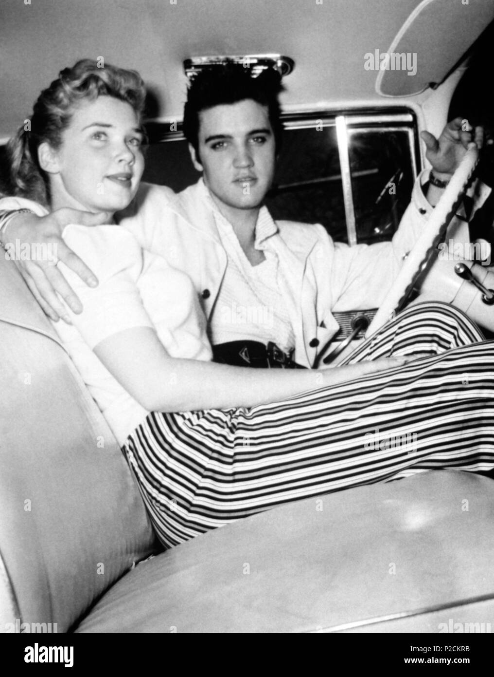 Cantante e attore Elvis Presley (1935-1977) si siede nel sedile del conducente di un auto con il suo braccio intorno a un misterioso giovane donna nel 1955. Foto Stock