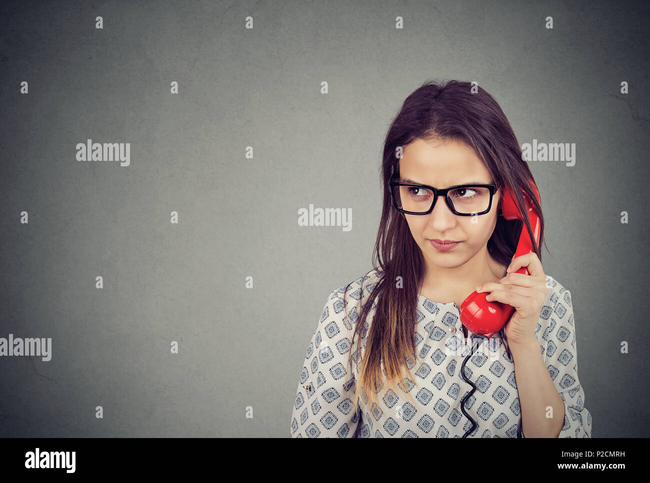 Giovane donna in occhiali parlando sul vecchio telefono che guarda lontano di incomprensione e di fastidio Foto Stock