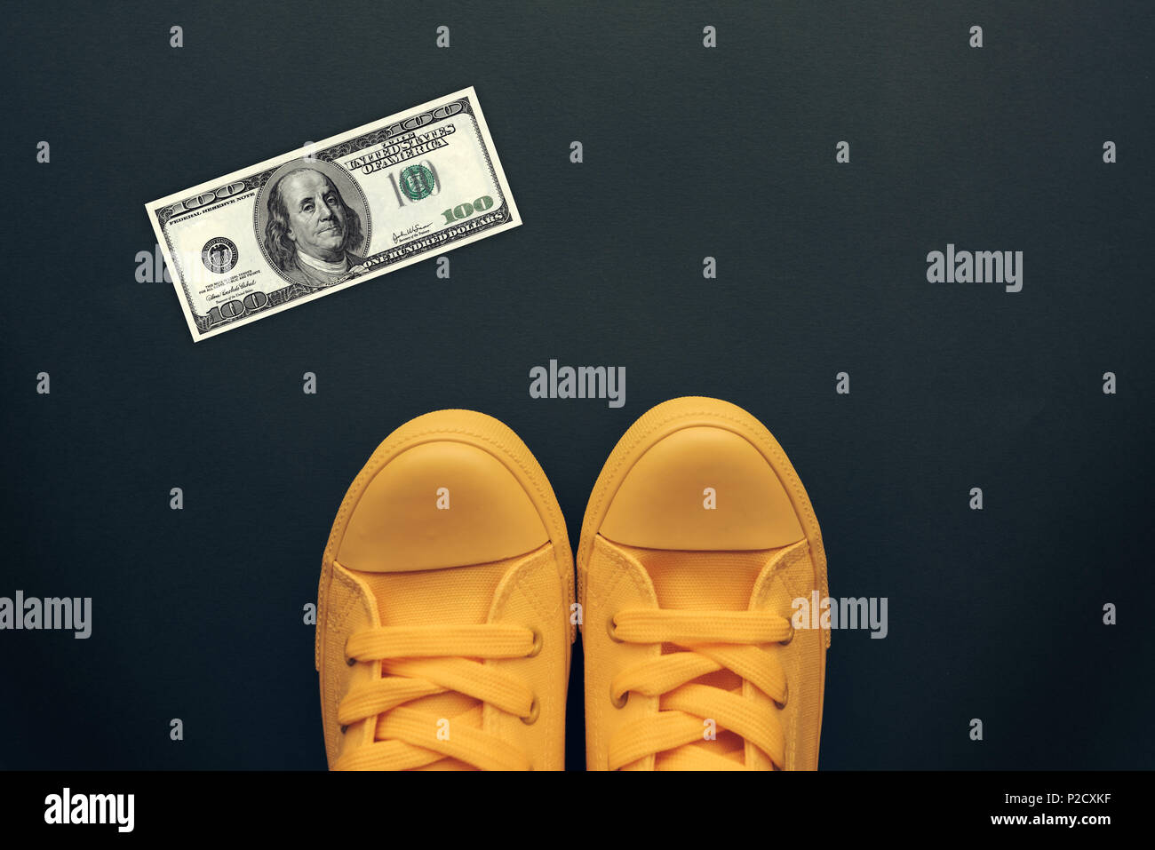 Trovato un centinaio di dollari sul pavimento, vista dall'alto del giovane in giallo sneakers in piedi sopra la carta moneta USA soldi bill Foto Stock