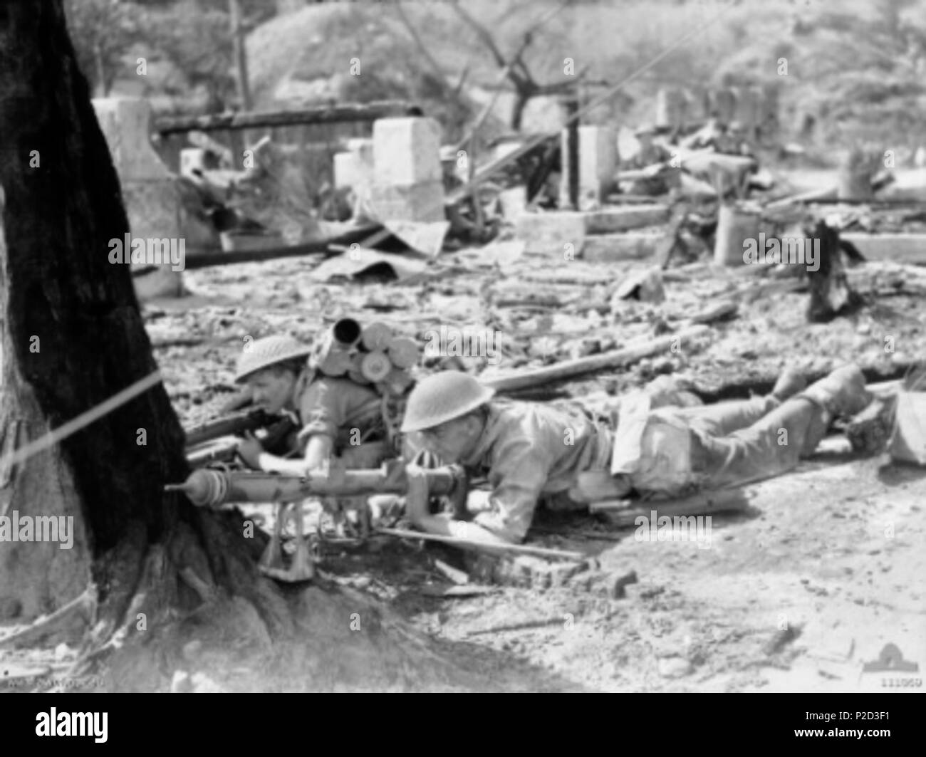 . IWM caption : SX27501 Private (PTE) Aubrey Carl Kotz (sinistra) e Pte W Spence (a destra), membri del plotone di 7, una società, 2/10 Battaglione prendere la copertura dietro ad un albero nella zona di città con i loro PIAT (proiettore, fanteria, Anti serbatoio) pistola durante l'oboe 2 Operazione. Commento : Questo era parte della battaglia di Balikpapan. Il 3 luglio 1945. Non dichiarato 5 Australian PIAT Balikpapan team Foto Stock