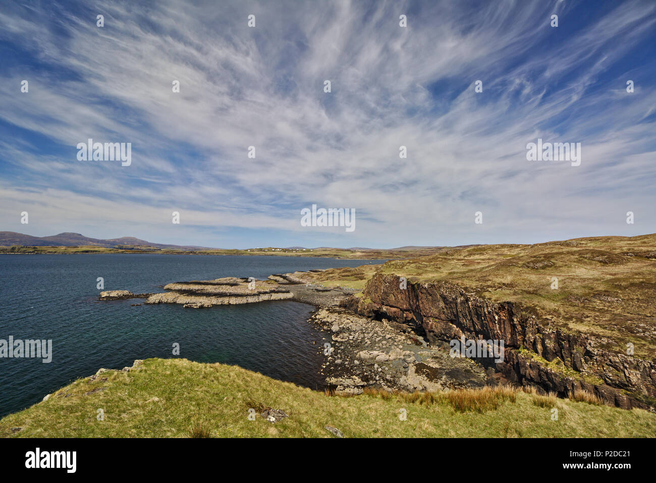 Scogliera sul mare con un basso promontorio in background e cielo blu con il bianco cirrus nuvole Foto Stock