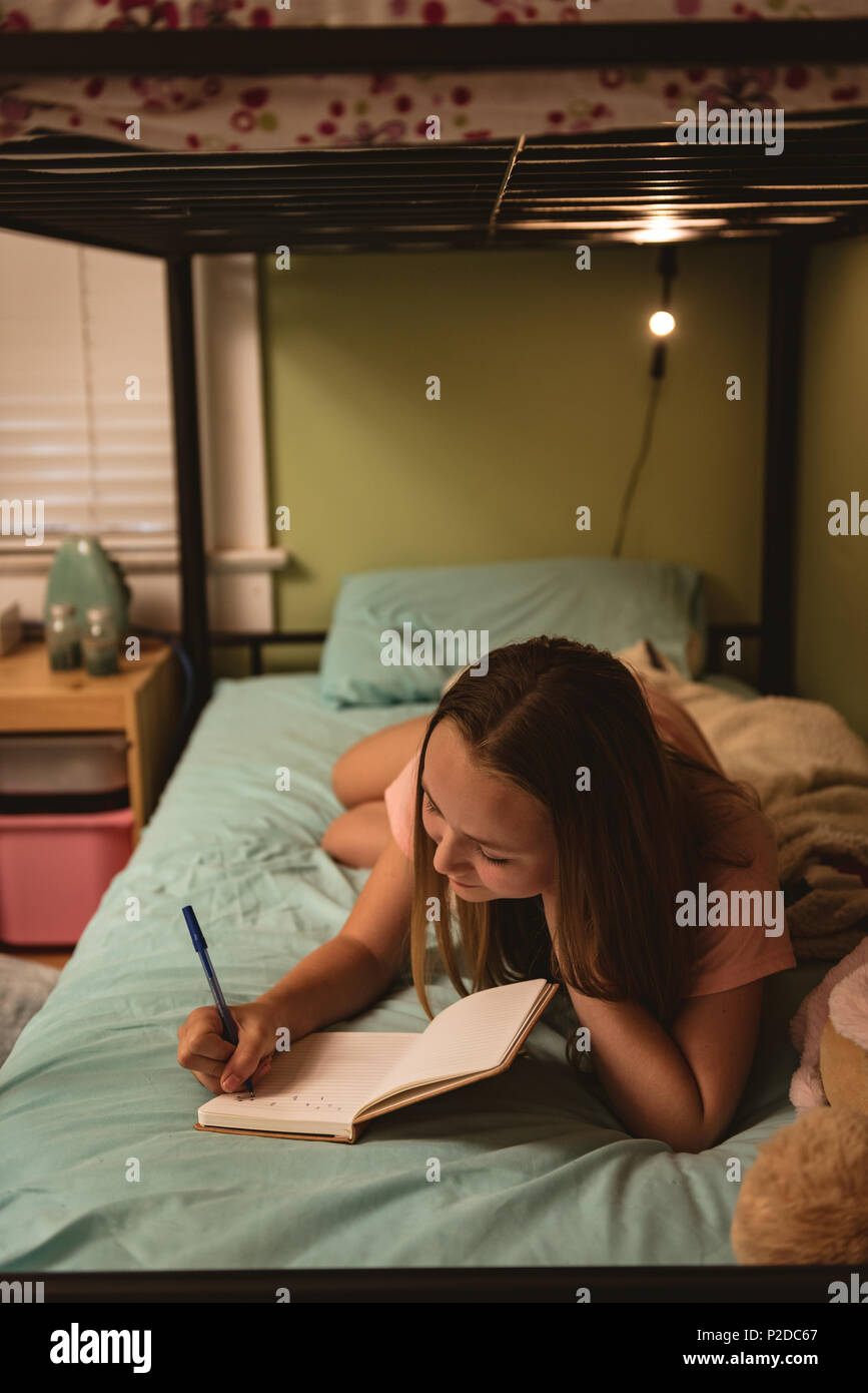 Ragazza distesa sul letto durante la scrittura del diario in camera da letto Foto Stock