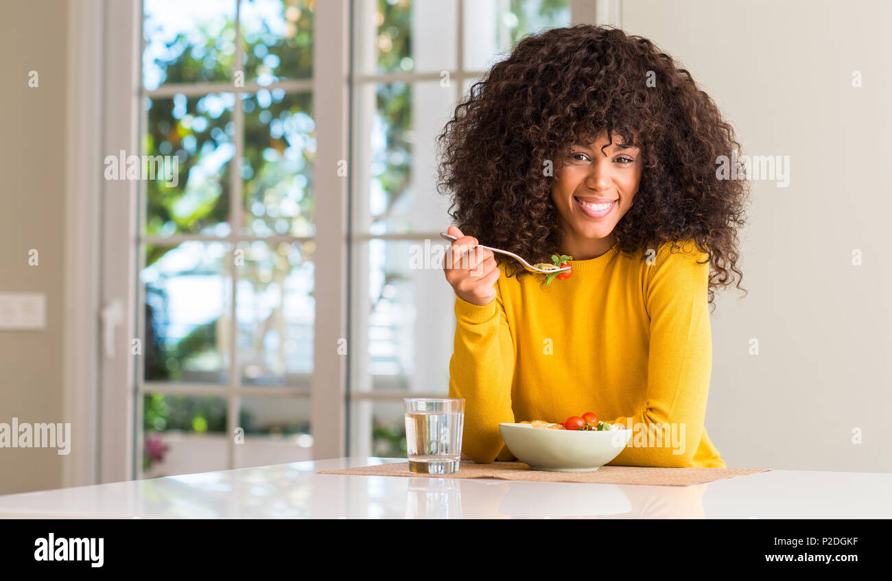 African American donna mangiare insalata di pasta con una faccia felice in piedi e sorridente con un sorriso sicuro che mostra i denti Foto Stock