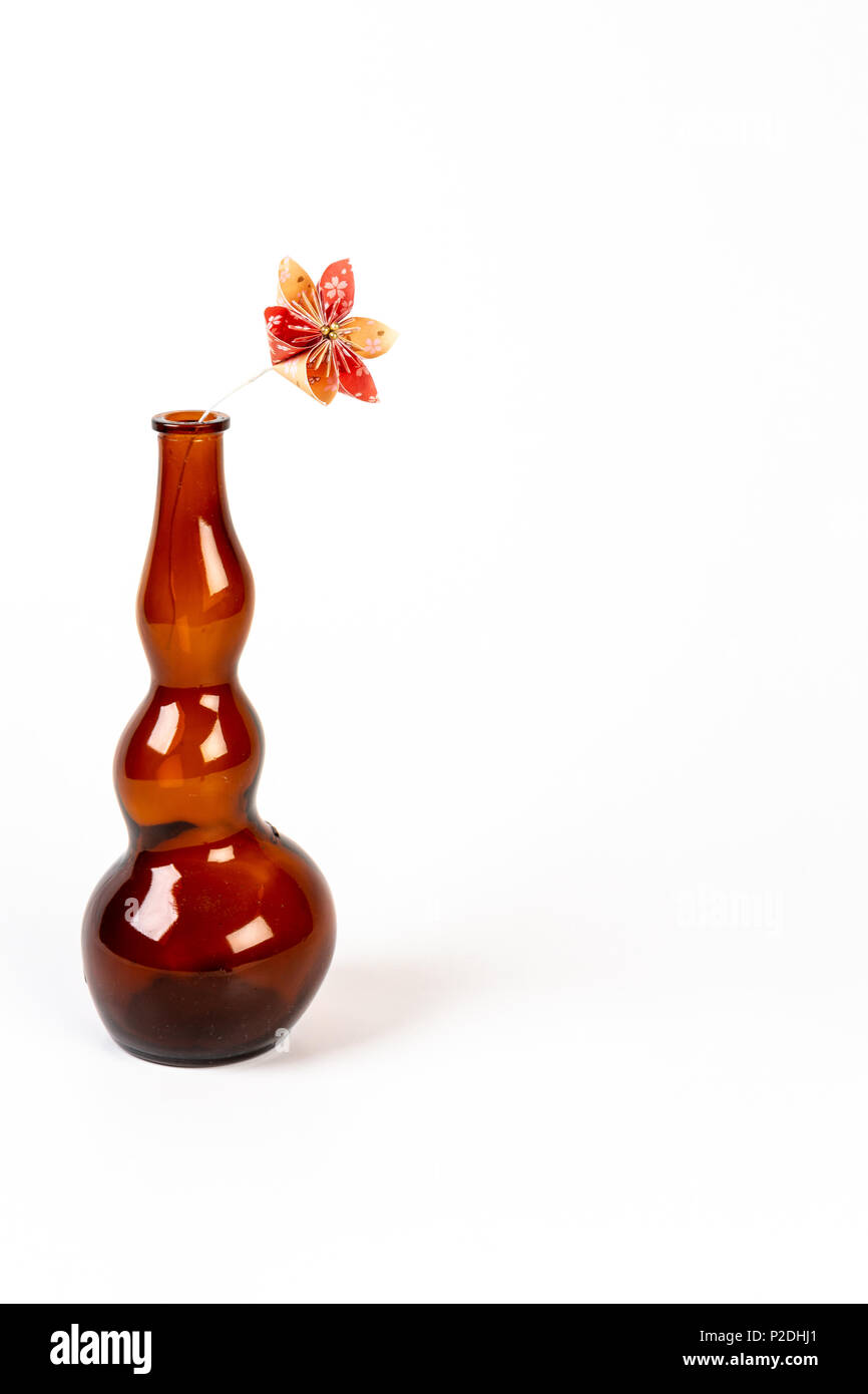 Close up di un arancio origami fiore in vetro scuro bottiglia su sfondo bianco. Foto Stock