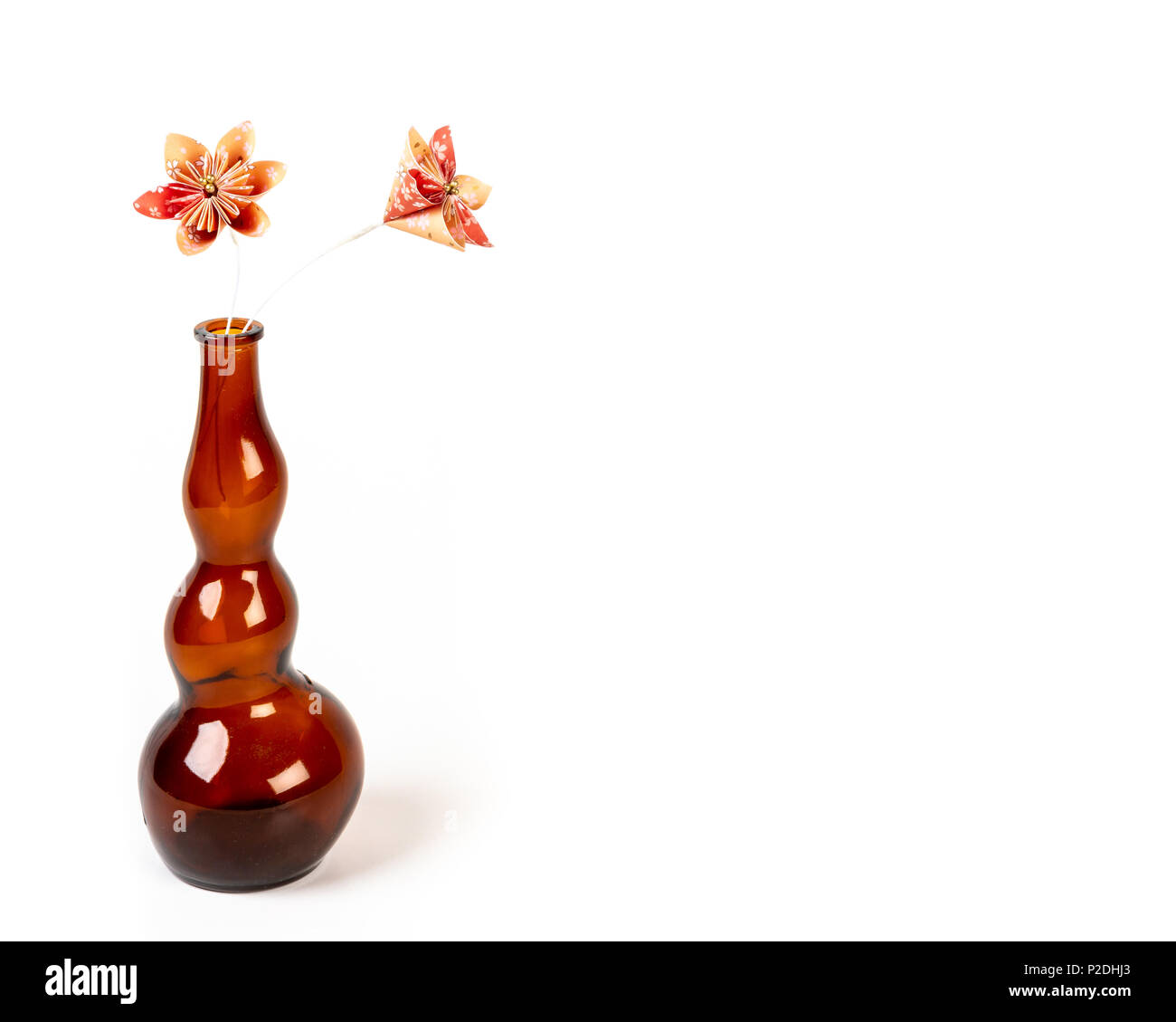 In prossimità dei due orange origami fiori in vetro scuro bottiglia su sfondo bianco. Foto Stock