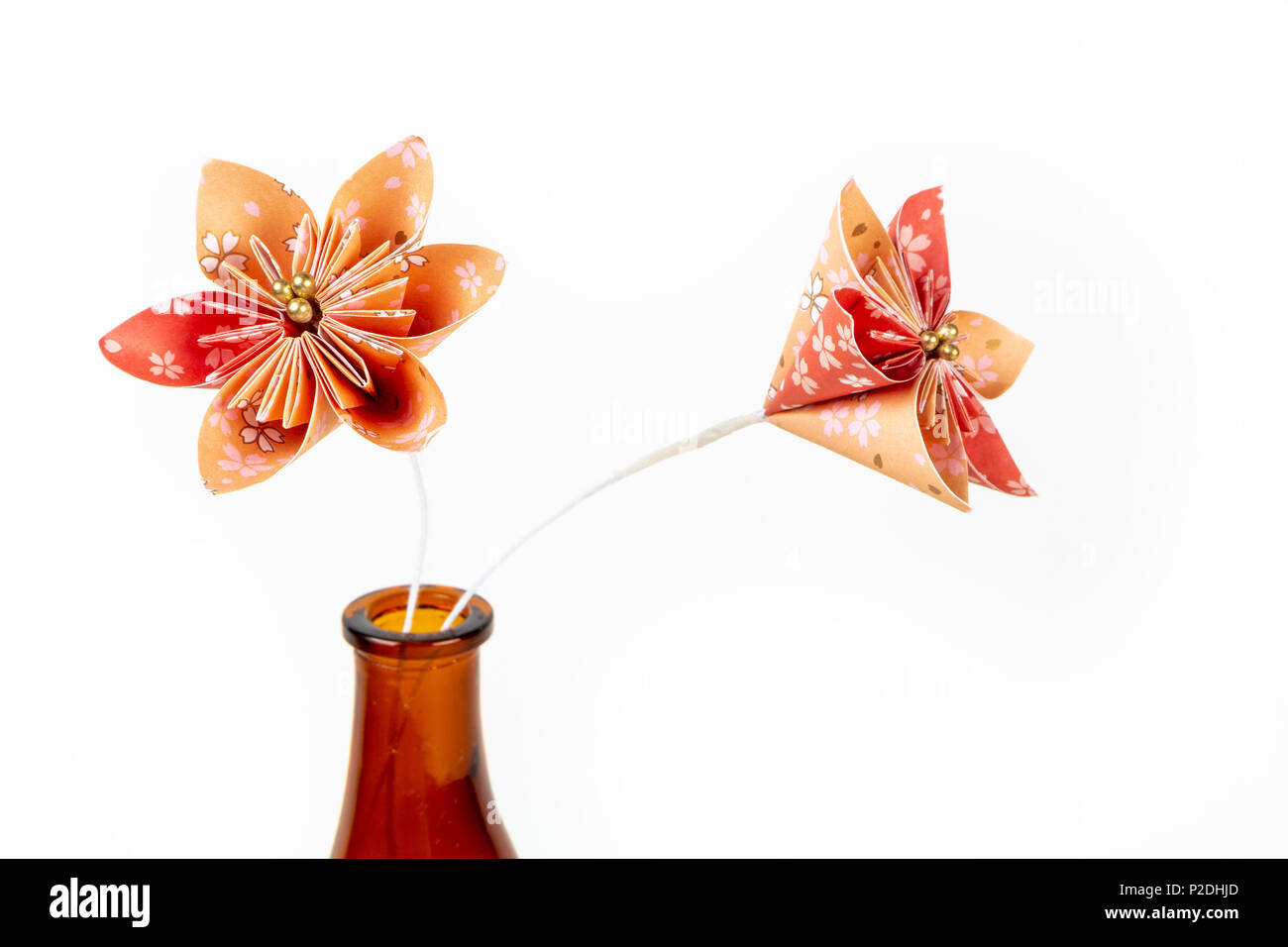 In prossimità dei due orange origami fiori in vetro scuro bottiglia su sfondo bianco. Foto Stock