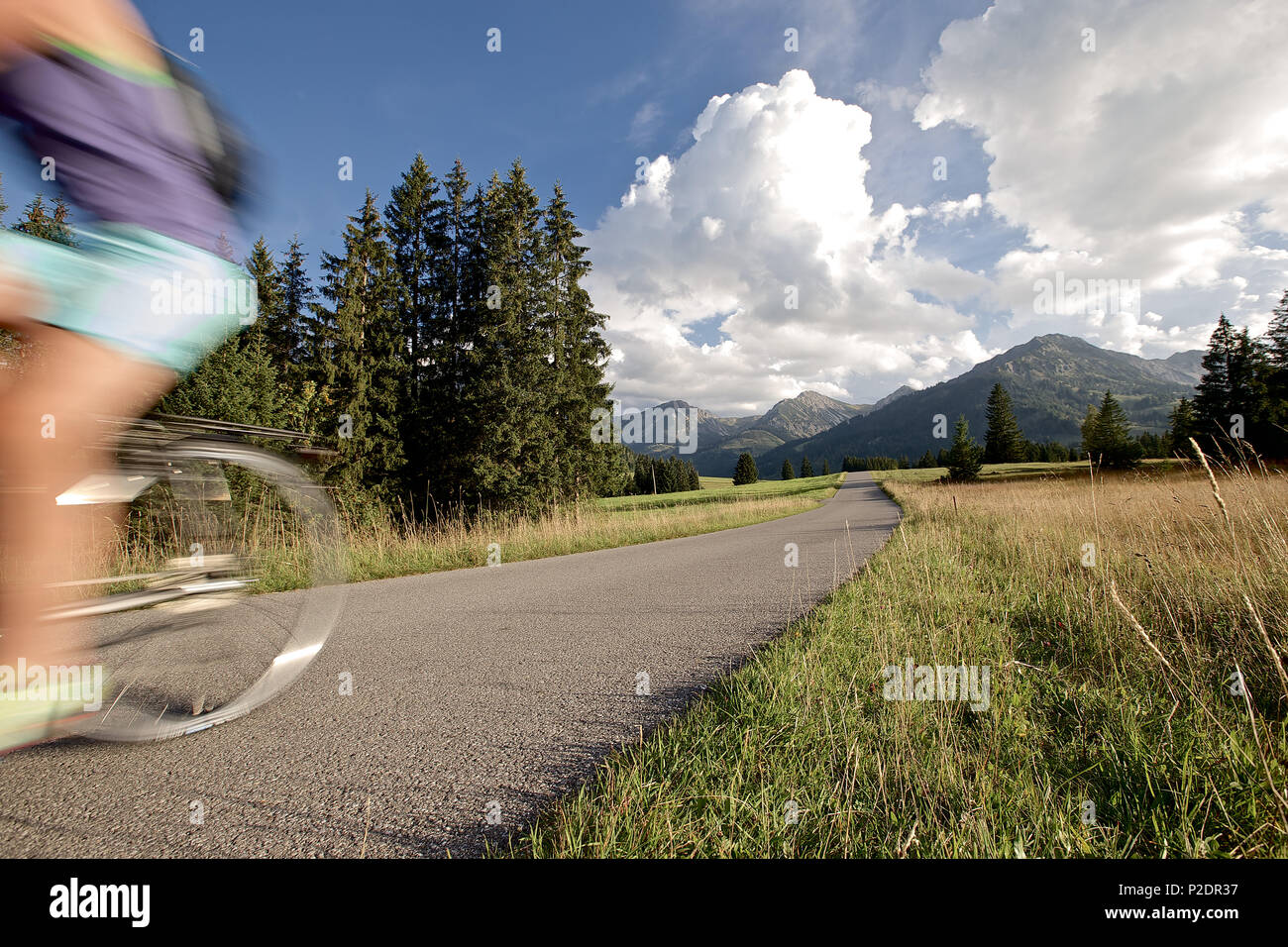 Giovane donna in sella la sua bici vicino alle montagne in una giornata di sole, Tannheimer Tal, Tirolo, Austria Foto Stock