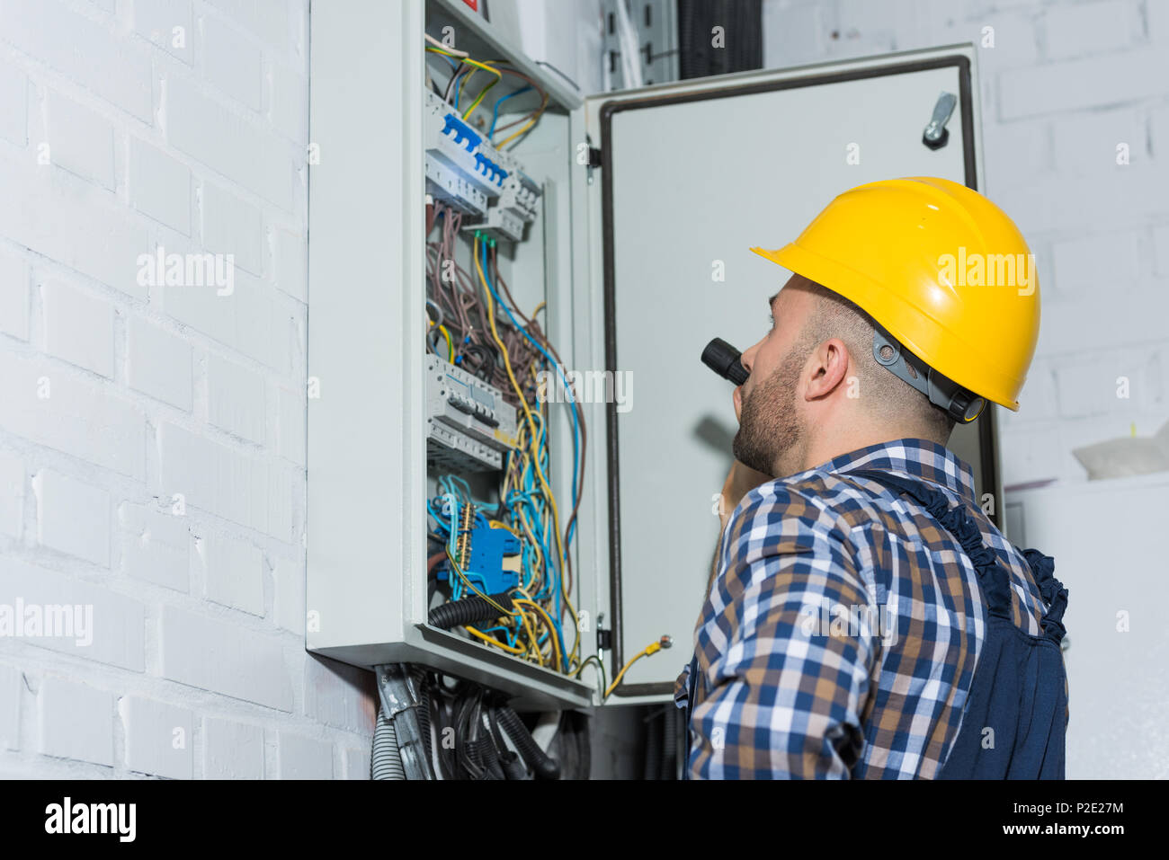 Elettricista professionale con torcia a lavorare dalla scatola del distributore Foto Stock