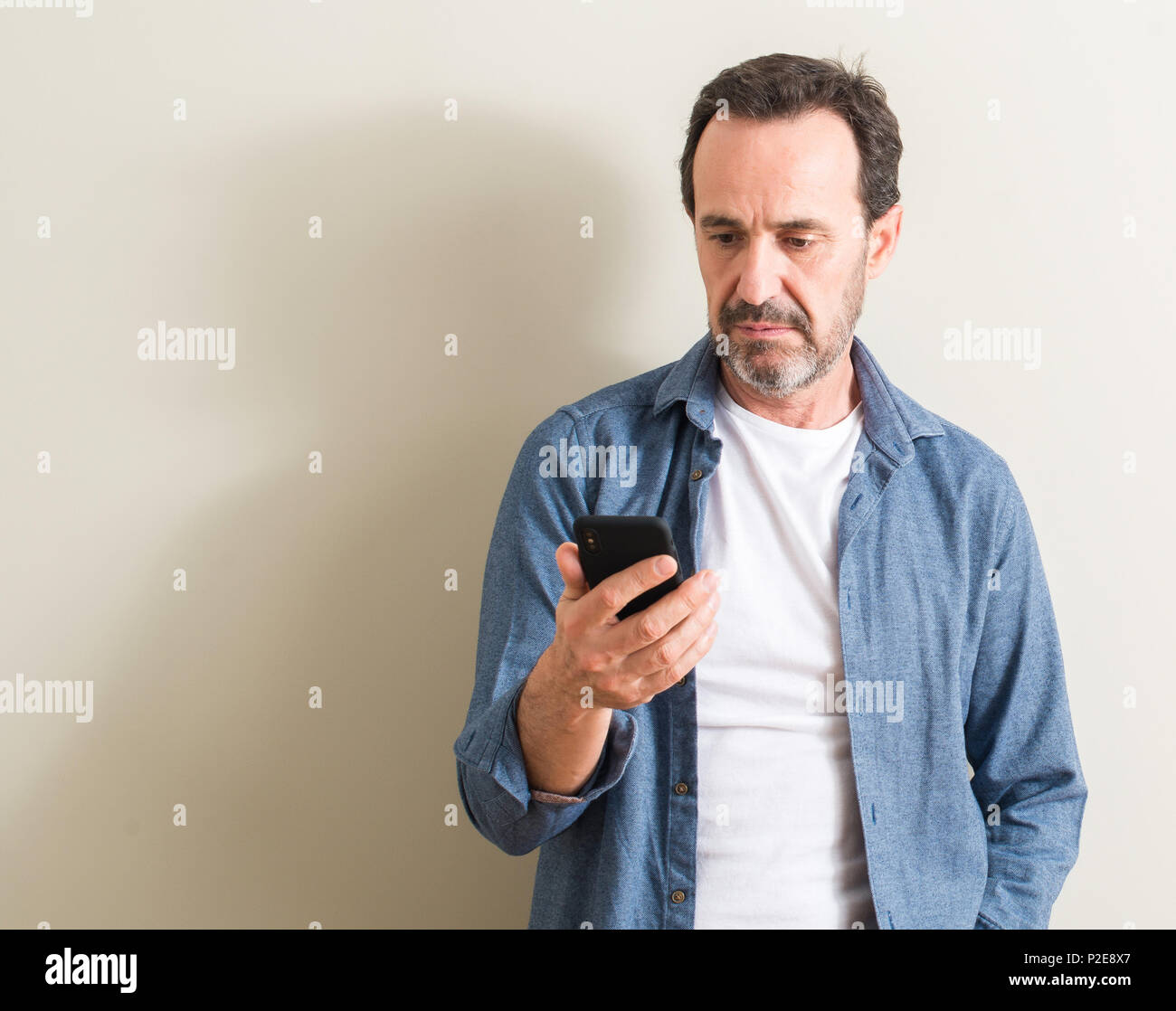 Senior uomo utilizza lo smartphone con un fiducioso espressione sul viso intelligente pensare grave Foto Stock