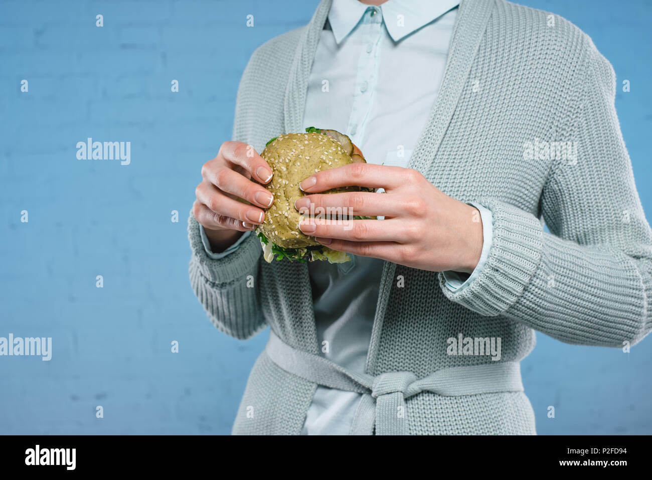Ritagliato colpo di donna azienda green vegan burger di fronte blu muro di mattoni Foto Stock