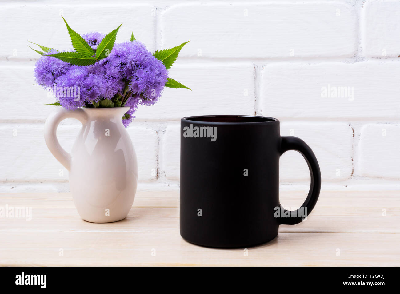 Nero caffè mug mockup con ageratum blu fiori nella rustica brocca. Boccale vuoto mock up per la promozione del brand. Foto Stock