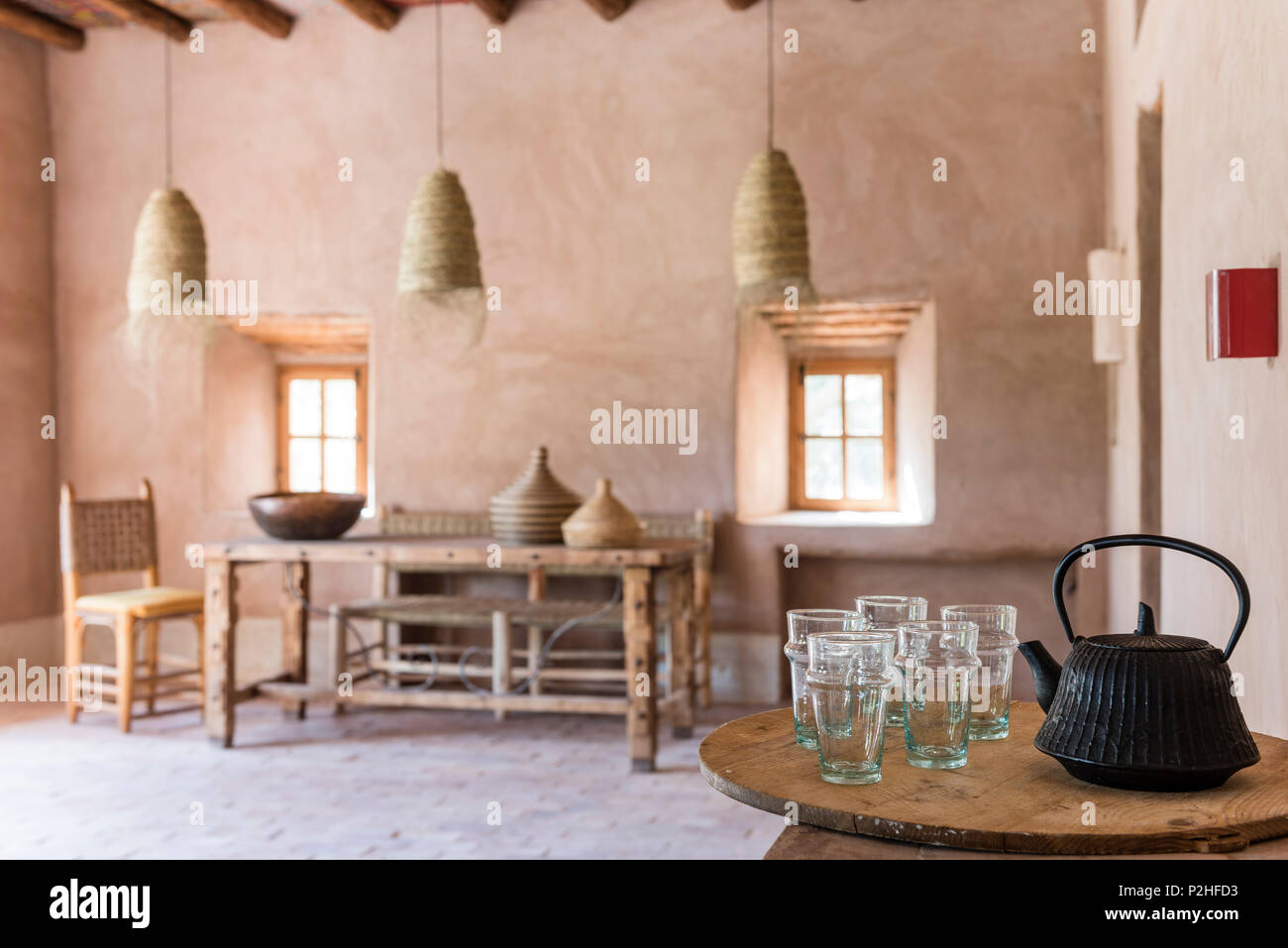 Ghisa teiera e bicchieri in primo piano del marocchino sala da pranzo con il rattan oendant luci, terra di pareti e pavimenti in terracotta Foto Stock