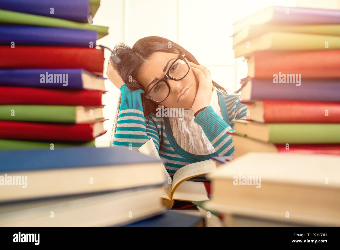 Stanco studente ragazza con gli occhiali seduto e apprendimento tra i molti libro in primo piano. Foto Stock