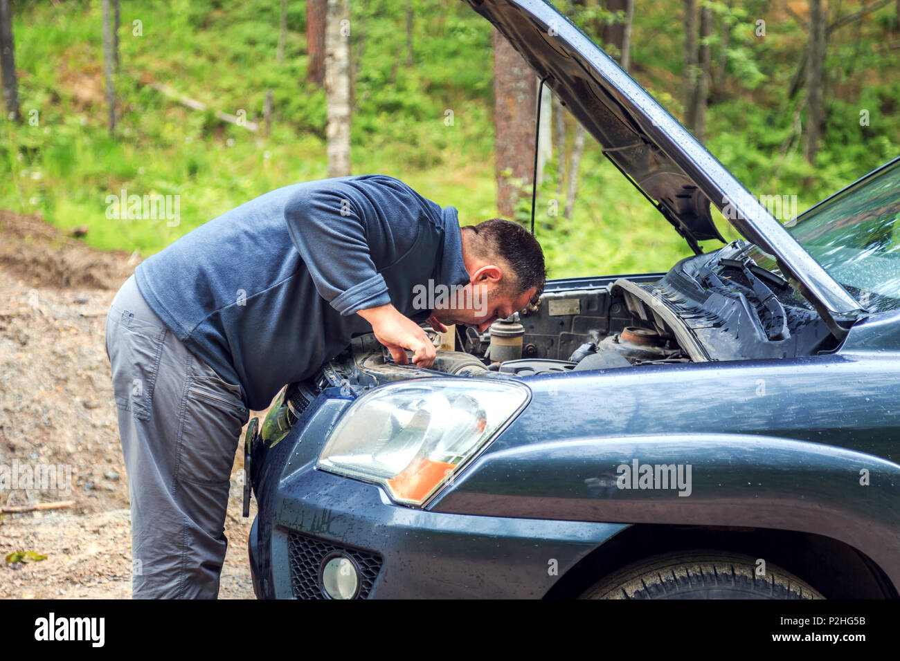 Stanco di riparazioni uomo rotto un auto. Strada della Foresta, Campagna. Foto Stock